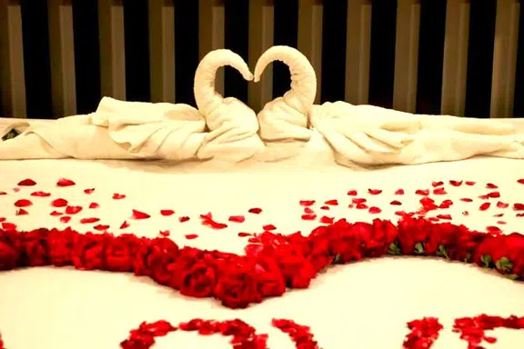 Lit décoré avec des serviettes en forme de cygnes et des pétales de roses pour un voyage de noces romantique.